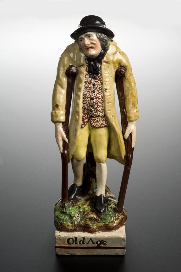 Pottery statue, entitled "Old Age" depicting a man on crutches