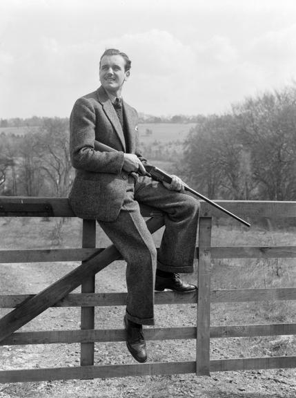 Man with a shotgun sitting on a gate