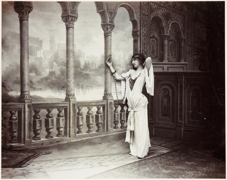 Woman in front of painted scenery
    A posed tableau photograph