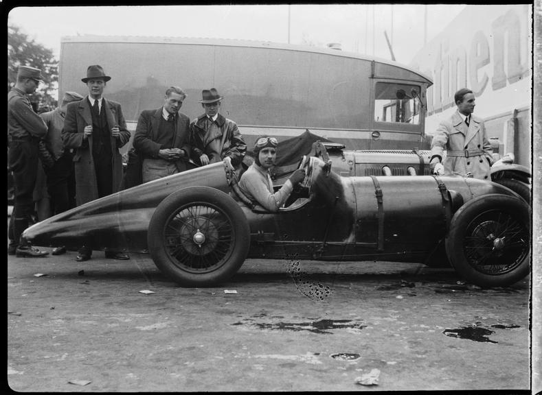 A driver at wheel of an Amilcar C6 racing car