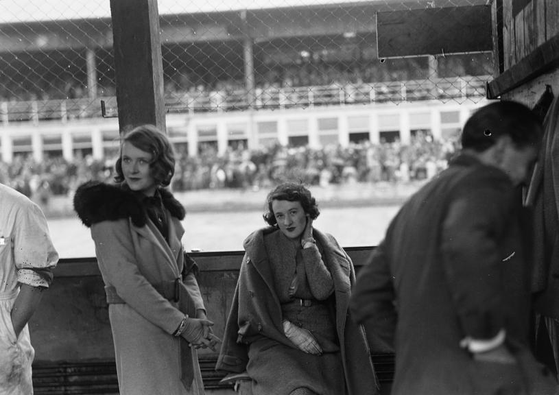 Two women pose by side of car racing track