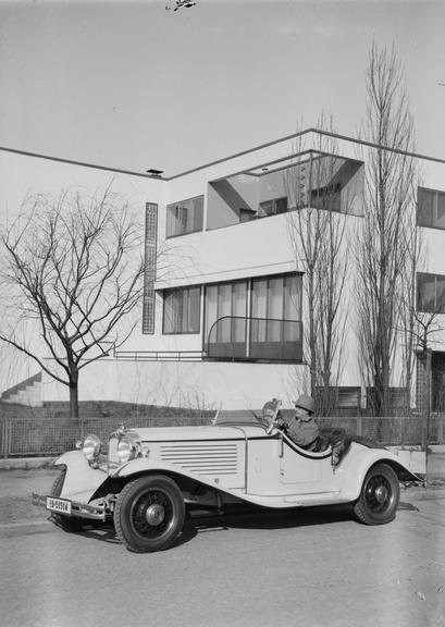 Couple in a car in front of a Modernist building