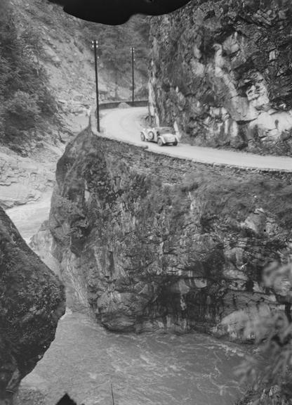 Car driving on a road cut into a mountain and above a river