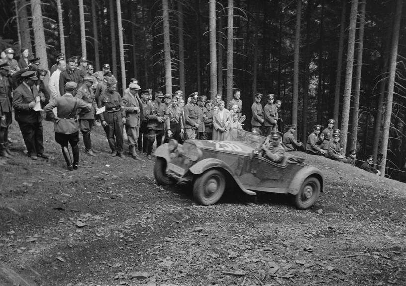 Car driving up a hill past spectators