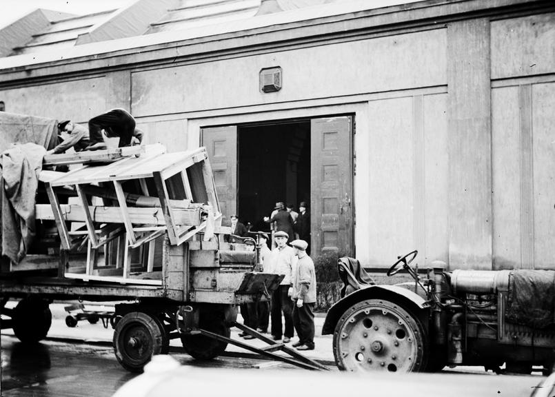 Men surrounding a tractor pulled cart with wooden structures