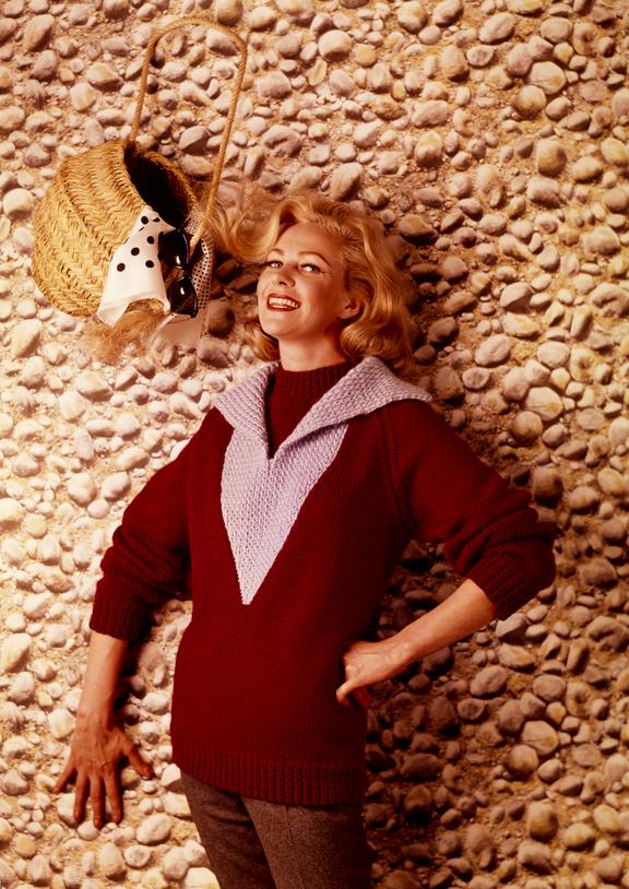 Woman wearing knitted jumper poses against cobbled "wall" with