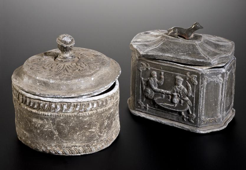 Left hand side: A4409, Lead tobacco jar, circular with detachable lid and finial in the form of a black person's head, moulded decoration, English, 1780-1850