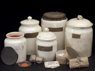 White ceramic jar with lid, containing white power, labelled "Sachm. Saturni"