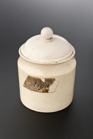 Ceramic jar with lid, containing brown plant flakes, labelled "Argal"