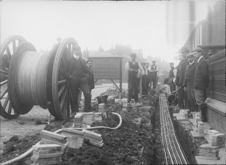 Works photographic negative of men laying cable in troughing