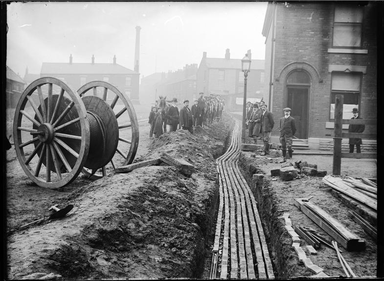 Works photographic negative of men laying cable in troughing