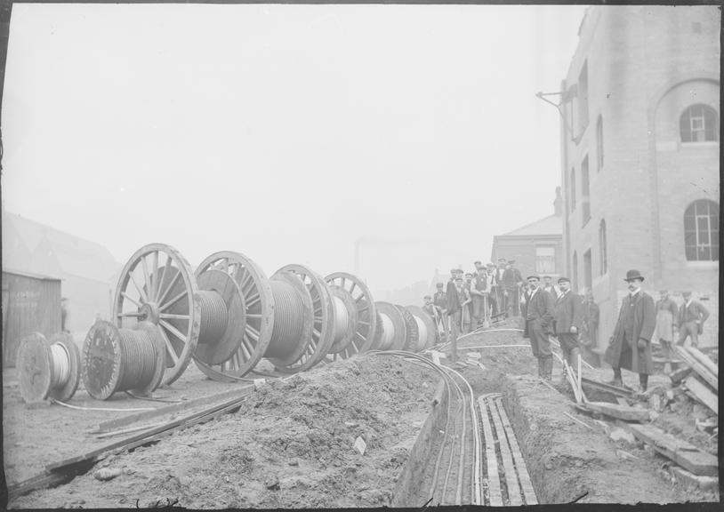 Works photographic negative of men laying cable in troughing