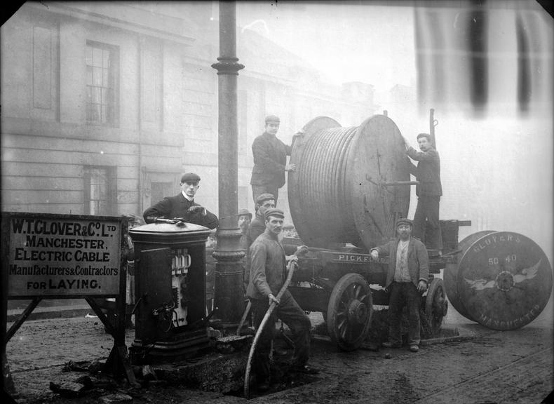 Works photographic negative of men feeding cable into man-hole