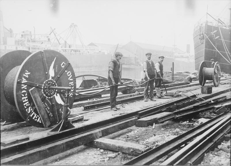 Works photographic negative of men feeding cable into manhole