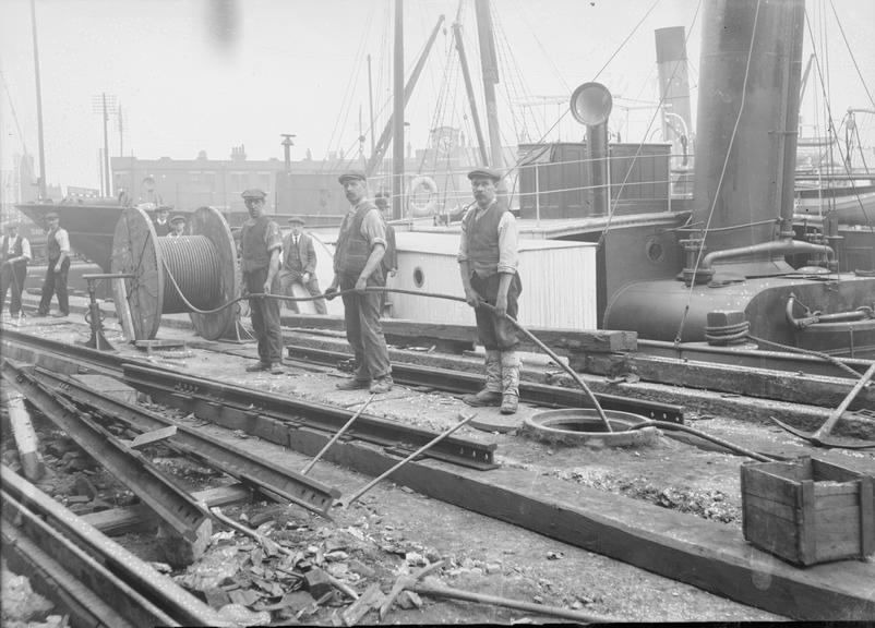 Works photographic negative of men feeding cable into manhole