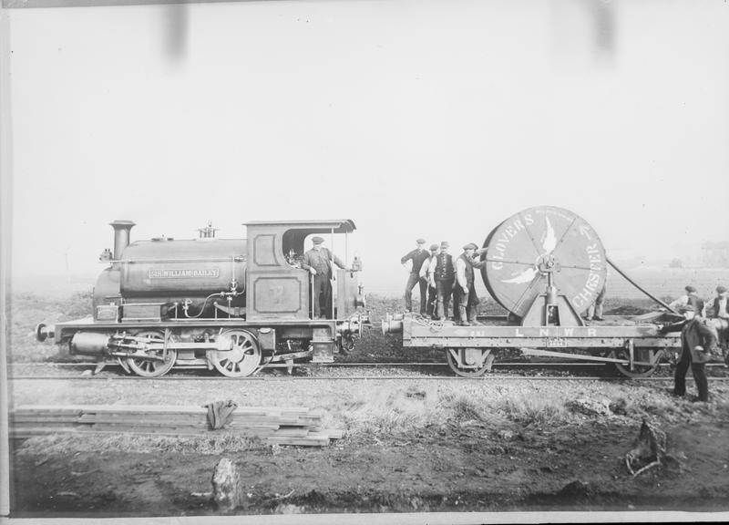 Shows cable drum on railway wagon coupled to 0-4-0 saddle-tank