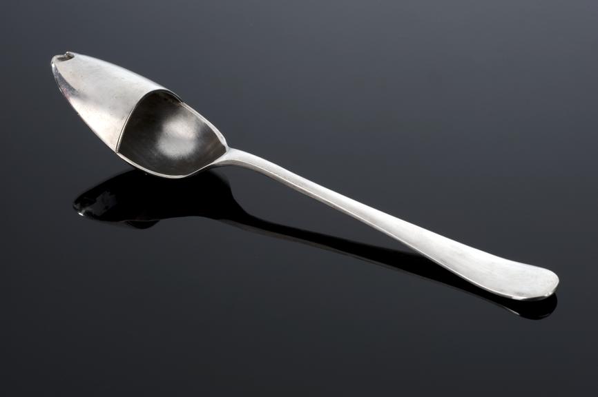 Silver medicine spoon, half covered, in original carton