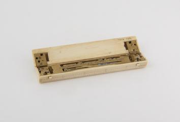 Ivory plotting scale opens to rolling parallel rule and contains dividers and combined pen and pencil