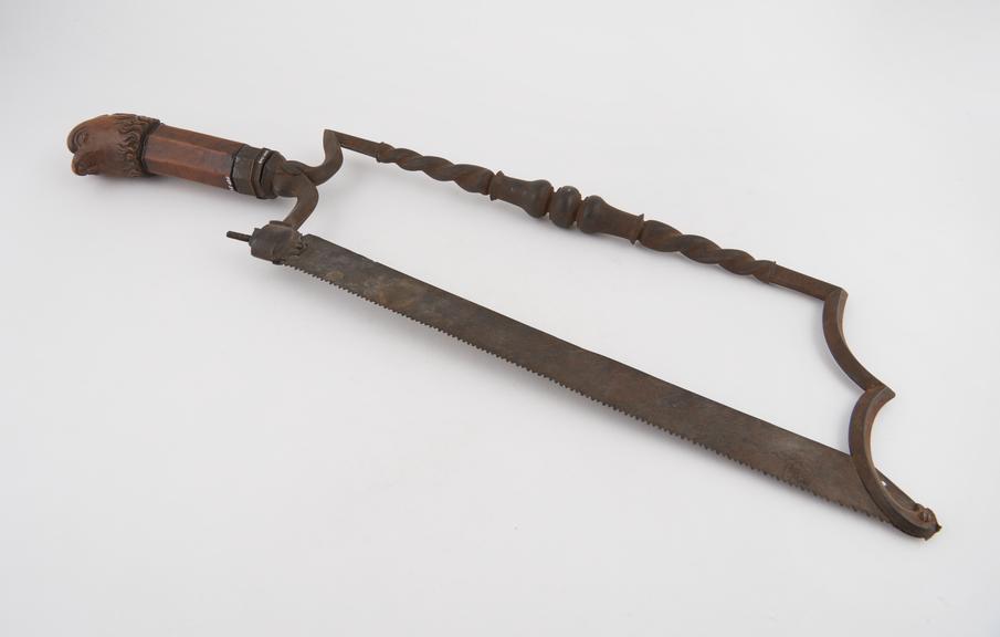 Bow-frame amputation saw with ornate carved wooden handle in