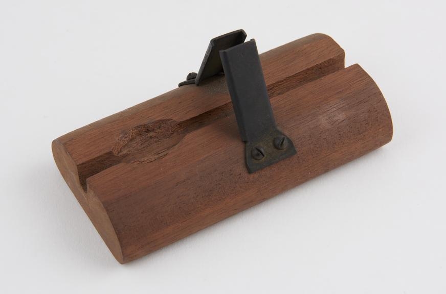 Block of wood with notch and metal clamp, used as stand