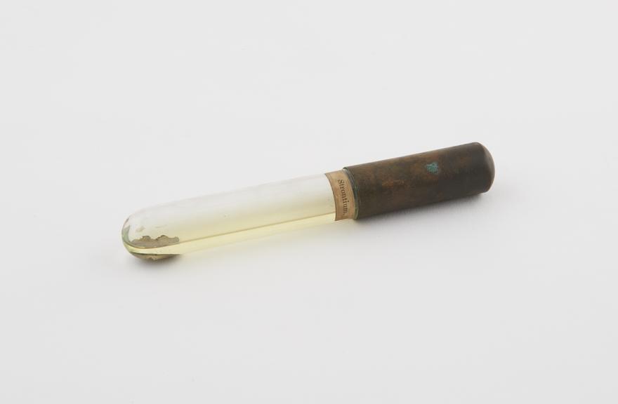 Glass vial with metal cap containing strontium regulus in rock