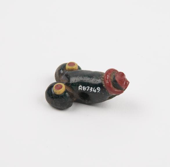 Amuletic pendant in form of male genitalia of moulded black glass with applied polychrome decoration (pendant)