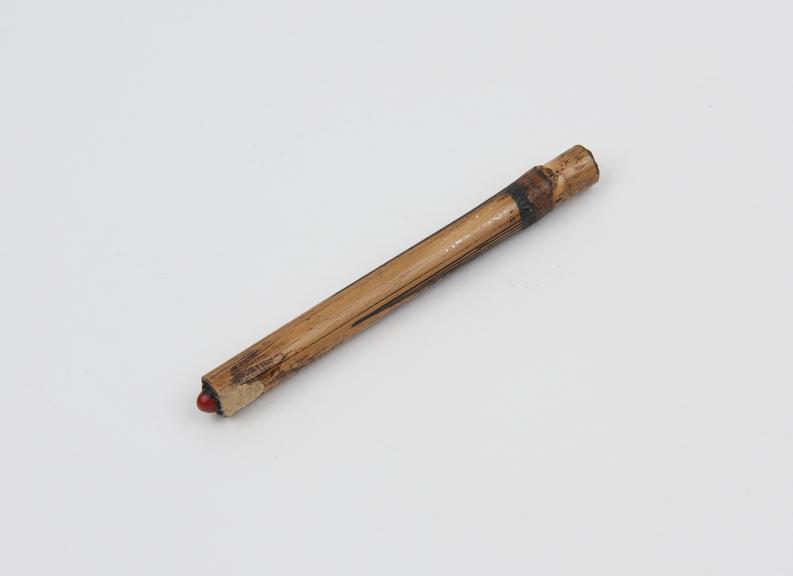 Nose pin consisting of length of bamboo with red seed inserted