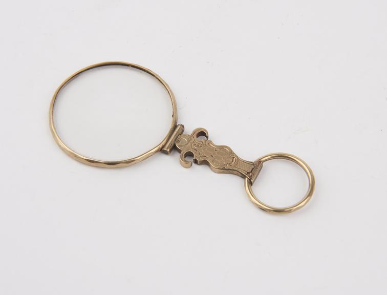 Single round eyeglass in decorated gold frame with handle.
