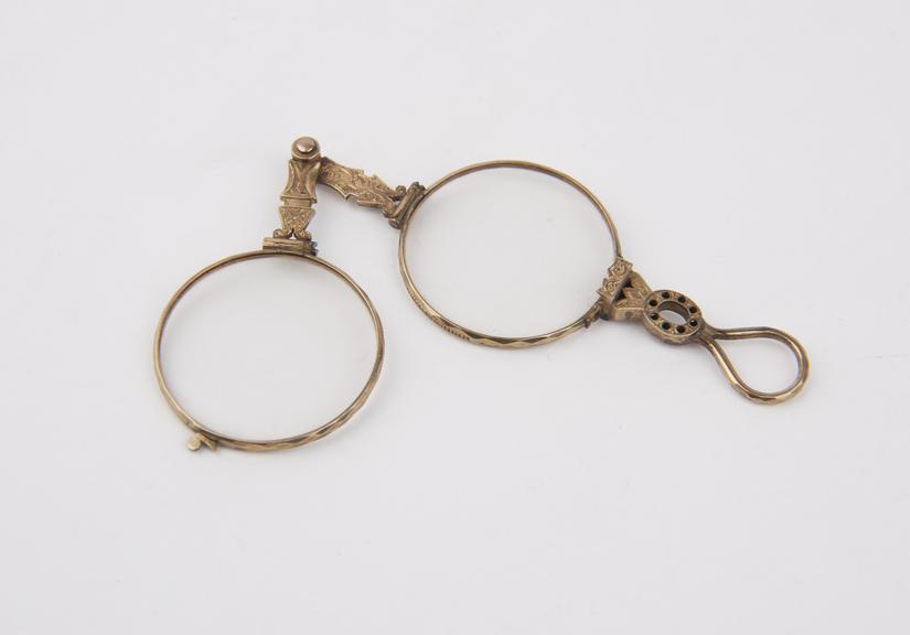 Ornamental gold pivot folding eyeglasses with round lenses.