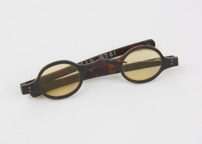 Pair of yellow-tinted spectacles with part of an arm missing