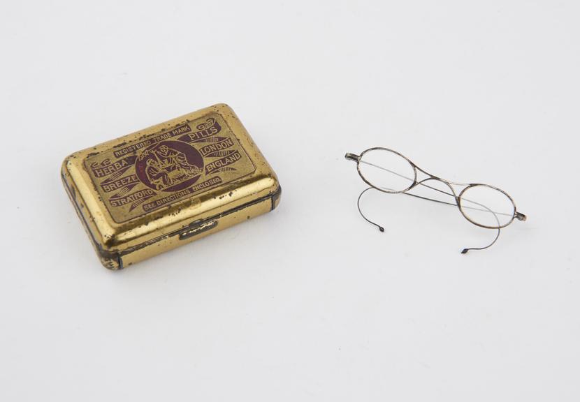 Pair of miniature spectacles stored a gold-coloured Herba Pills