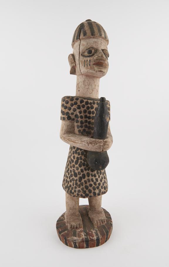 Painted wooden carving of human figure wearing black spotted