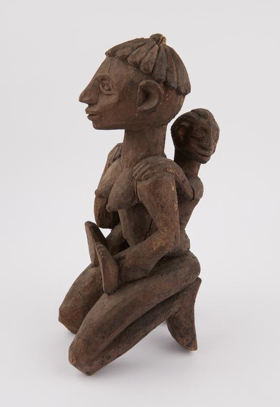 Carved wooden figure of kneeling woman holding child on her