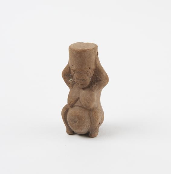 Terracotta pendant in form of squatting pregnant female with object on head