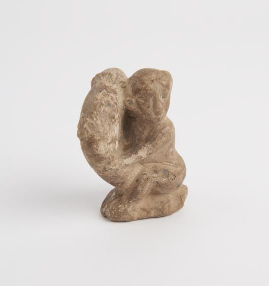 Small terracotta figure of a squatting male supporting priapus over right shoulder