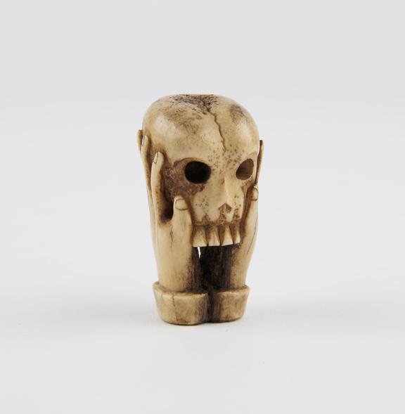 Bone sculpture of a skull, supported by two hands