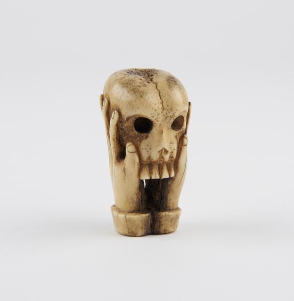 Bone sculpture of a skull, supported by two hands