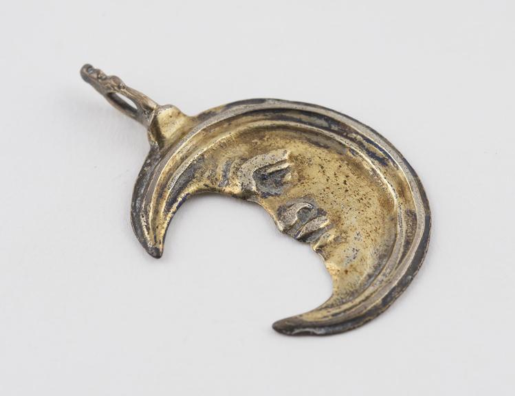 Silver gilt amulet, in form of a crescent moon with a face