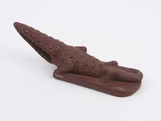 Red earthenware skin scraper in form of crocodile