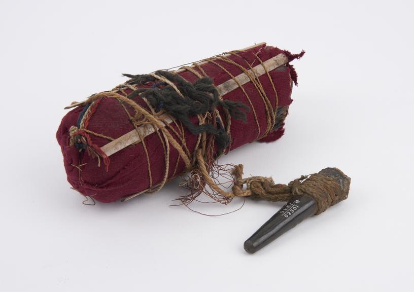 Bundle of sticks covered in red cotton cloth and bound with string and splints of wood