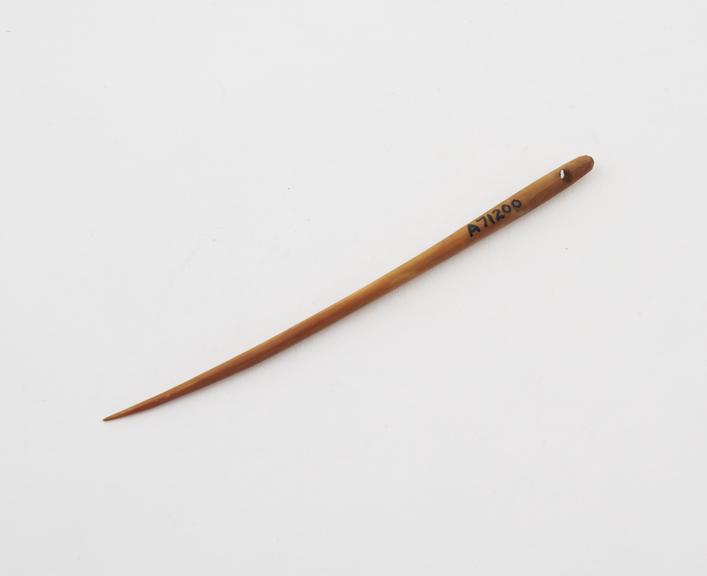 Ivory needle with eye at top, slightly curved towards tip