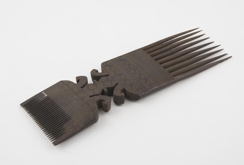 Double-pronged comb of black hardwood with elaborately carved