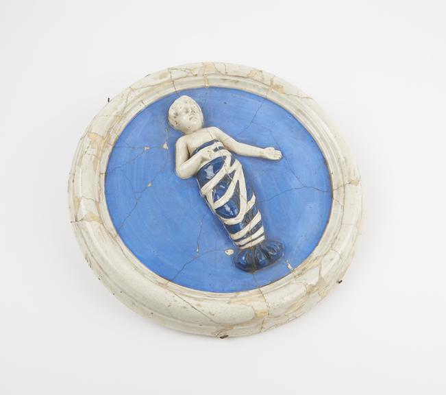 Circular porcelain plaque depicting child in swaddling clothes