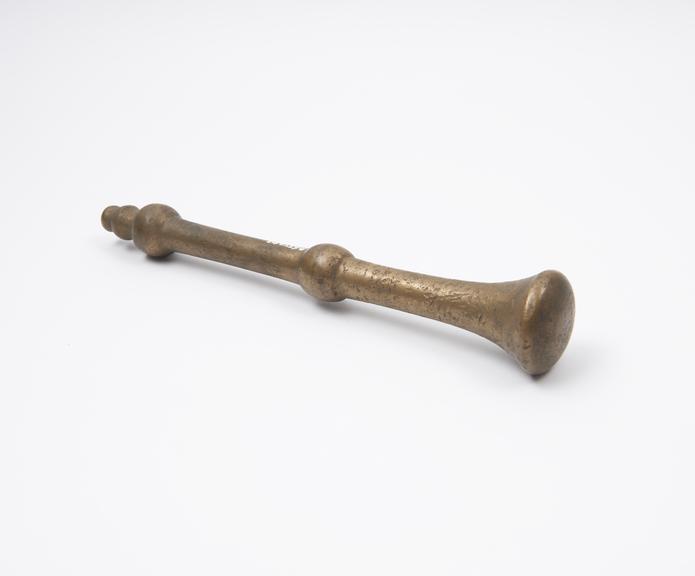 Distorted brass pestle with flange and triple-knob finial