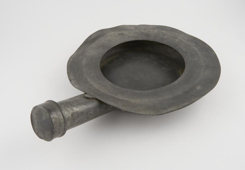 Circular pewter bedpan, with large flat rim and straight handle