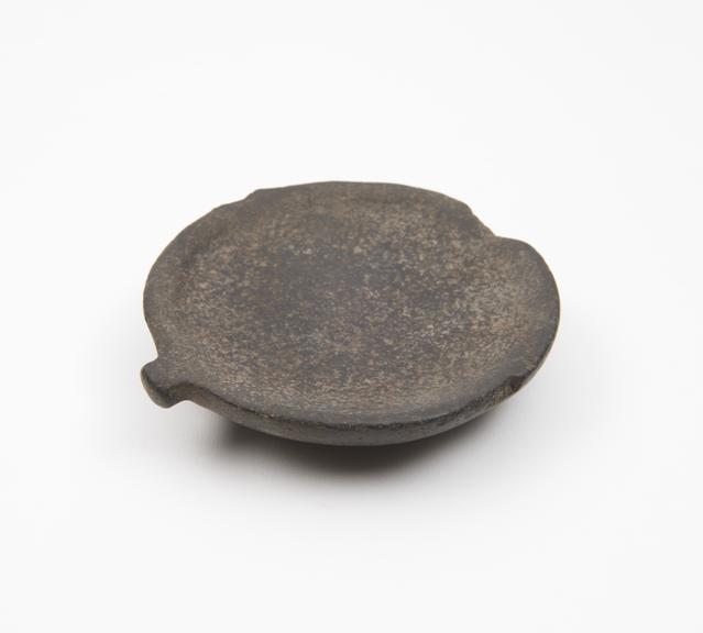 Shallow saucer-like palette, in pitted black stone