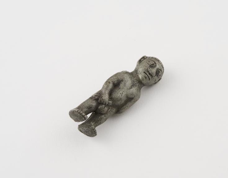 Small metal phallic figure of male holding penis with one hand