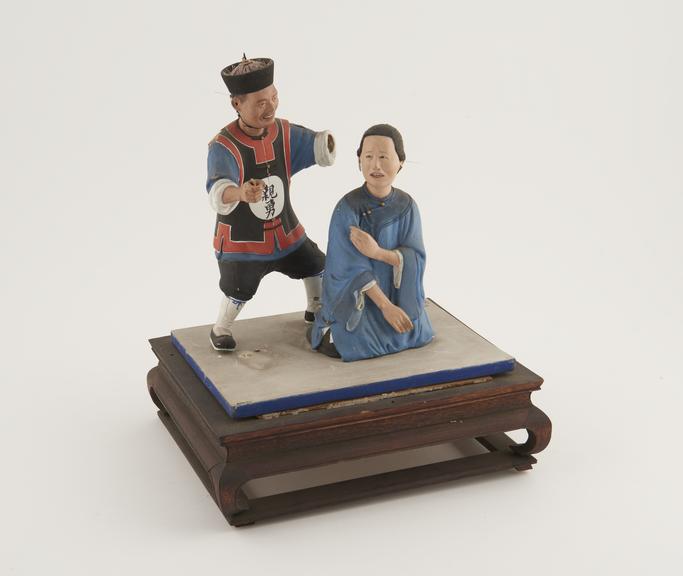 Painted wooden figures depicting man striking woman criminal or