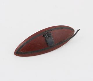 Pointed oval hair slide of ochre-coloured Parkesine, shield in centre