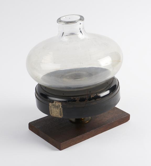 Thick glass flask on wooden base on a short brass pillar on a